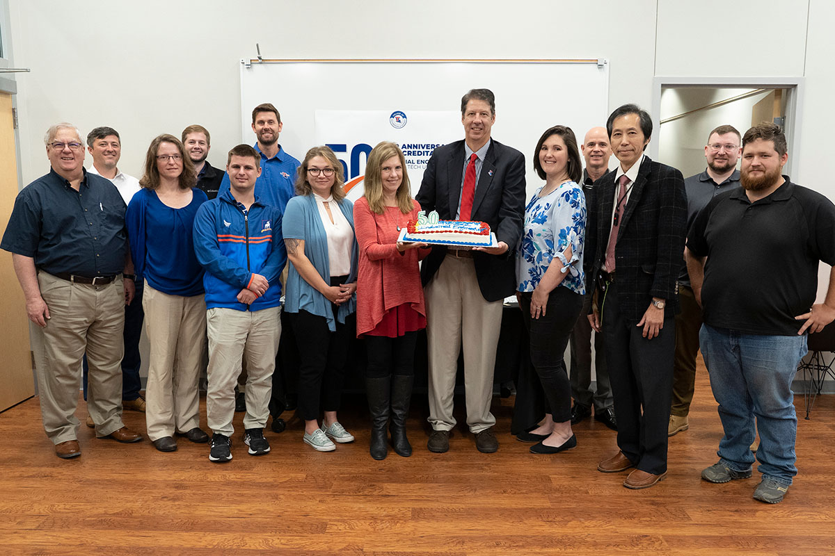 Industrial Engineering faculty, board members, and students celebrating with a cake